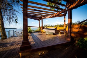 A wooden deck with a grill and seating area overlooking a body of water.