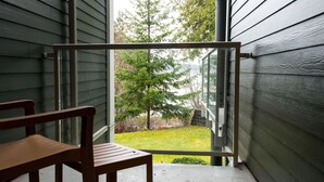 A wooden chair on a balcony with a view of a green lawn and trees. - Ocean Tide (Unit A+B) - Waterfront Condo - Sleeps 6 - Pool - Family (Nanoose Bay)