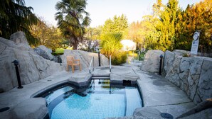 A stone pool with a tiled edge, surrounded by rocks and a wooden chair. - Ocean Tide (Unit A+B) - Waterfront Condo - Sleeps 6 - Pool - Family (Nanoose Bay)