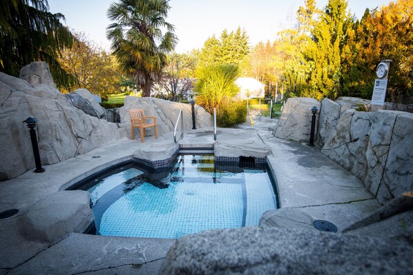 A stone pool with a tiled edge, surrounded by rocks and a wooden chair.