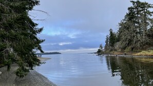 A calm lake with a pebble beach, surrounded by dense trees. - Ocean Tide (Unit A+B) - Waterfront Condo - Sleeps 6 - Pool - Family (Nanoose Bay)