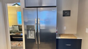 Un refrigerador de acero inoxidable con dos puertas, un dispensador de agua, una tabla de cortar de madera encima y un gabinete azul oscuro abajo.