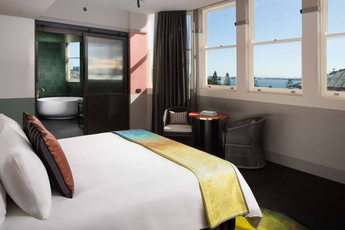 Habitación de hotel con cama, una silla, una mesita, ventana con vistas y baño con bañera.