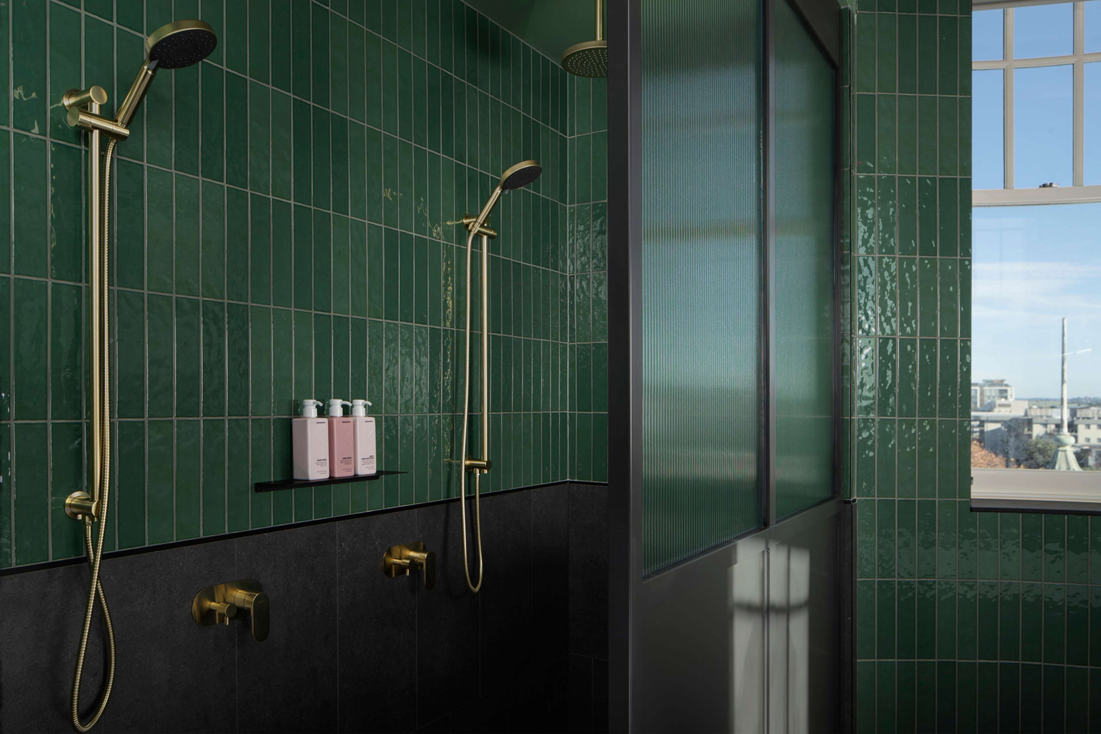 A bathroom with green tiled walls, a window, and a shower with a gold faucet.