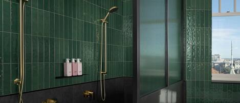 A bathroom with green tiled walls, a window, and a shower with a gold faucet.