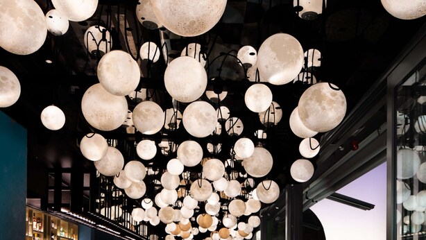 A modern bar area with a unique ceiling design featuring spherical light fixtures, a bar counter, and seating with a patterned floor. - QT Newcastle (Newcastle)