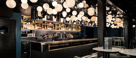 A bar area with a black counter, multiple hanging spherical light fixtures, and a variety of bottles on shelves.