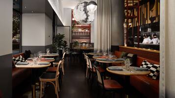 A restaurant with round tables, cushioned booths, and a bar area.