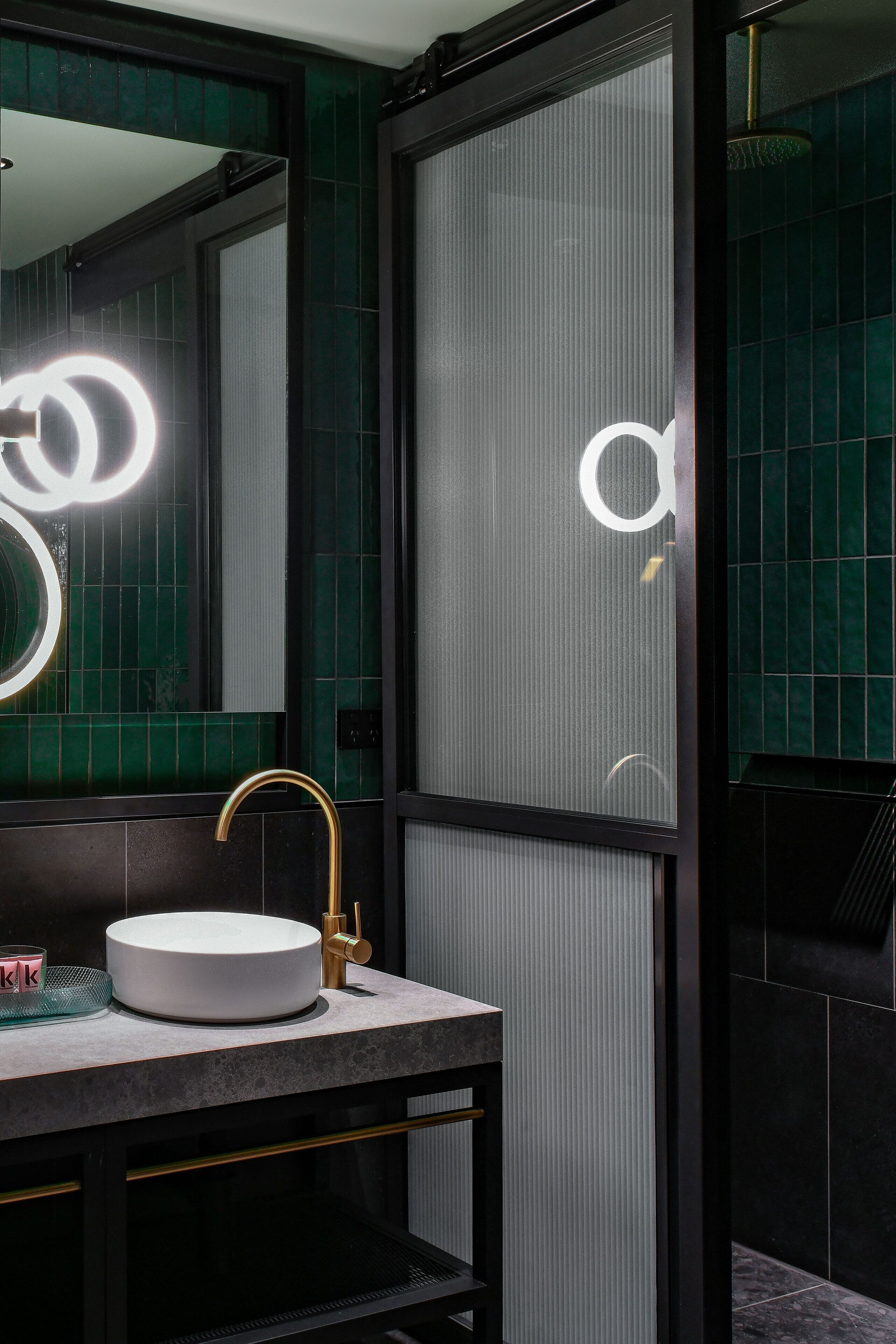 A modern bathroom with a round sink, gold faucet, and a large mirror.