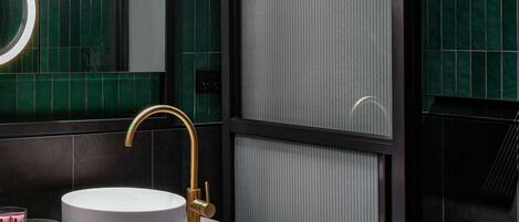 A modern bathroom with a round sink, gold faucet, and a large mirror.