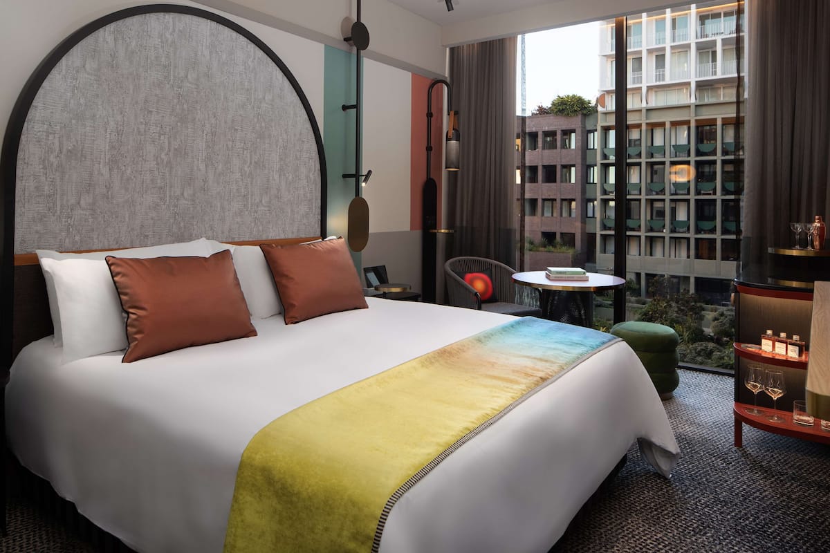Una habitación de hotel con una cama grande, vistas a la ciudad y una pequeña mesa con una lámpara.
