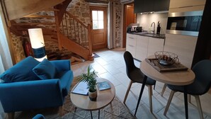 A cozy living room with a blue sofa, a small round table with a plant, and a staircase leading to a kitchen area with modern appliances. - Quercy cottage, charm, comfort, garden with trees, natural swimming pool (Frontenac)