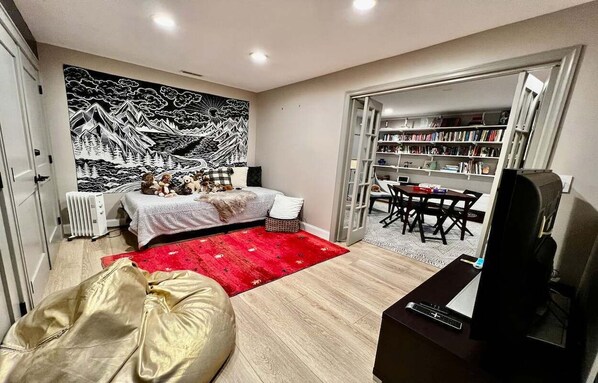 Un espacio habitable compacto con cama, alfombra roja, sofá, televisor y estantería.