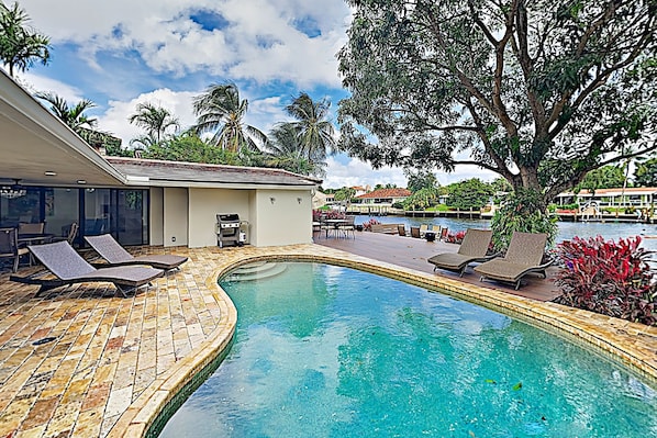 A pool area with lounge chairs, a small building, and palm trees.