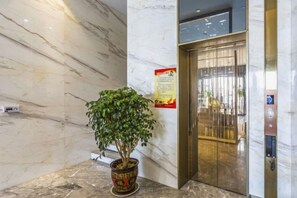 Una pared de mármol, una planta en maceta y la puerta de un ascensor.