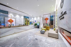 Un vestíbulo de hotel con mostrador de recepción, zona de estar y un espejo grande que refleja el interior.