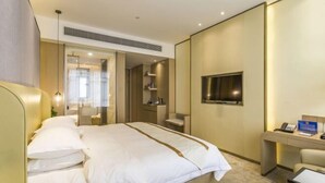 Habitación de hotel con cama, escritorio, televisor y baño visible a través de una puerta abierta.