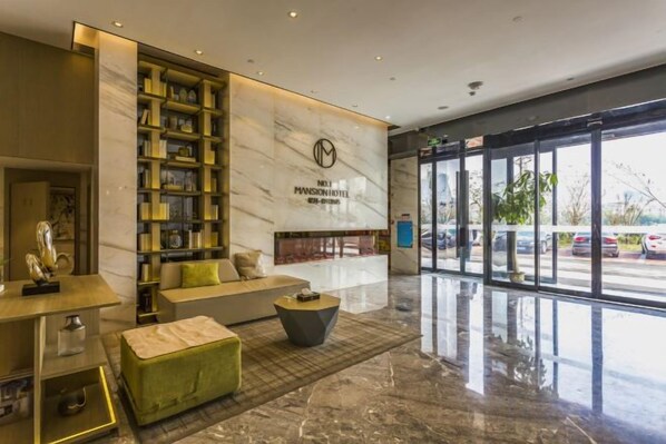 Un vestíbulo de hotel con una recepción, zona de estar y un amplio ventanal con vistas a la calle.