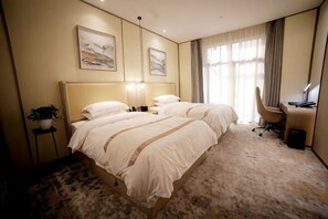 Ein Hotelzimmer mit zwei Betten, einem Schreibtisch, einem Stuhl und einer Zimmerpflanze.