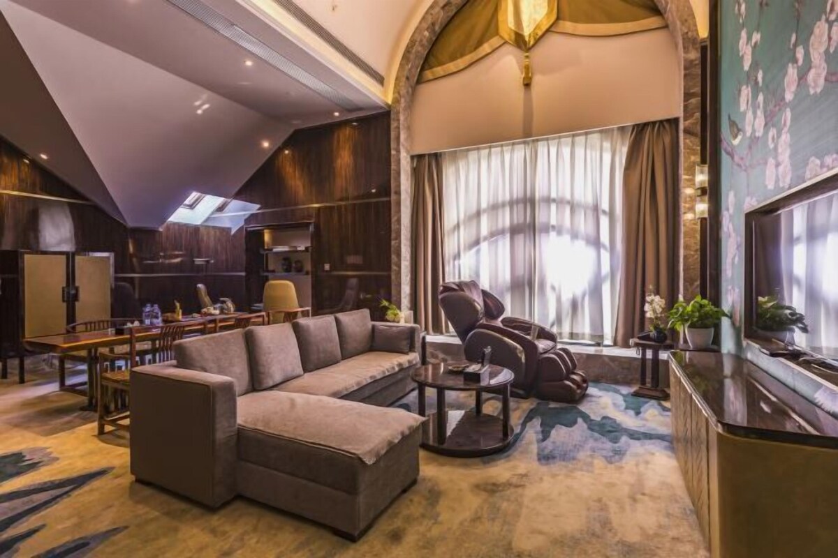 Una sala de estar moderna con un sofá modular, un sillón de masaje, una mesa de centro y un ventanal con cortinas.