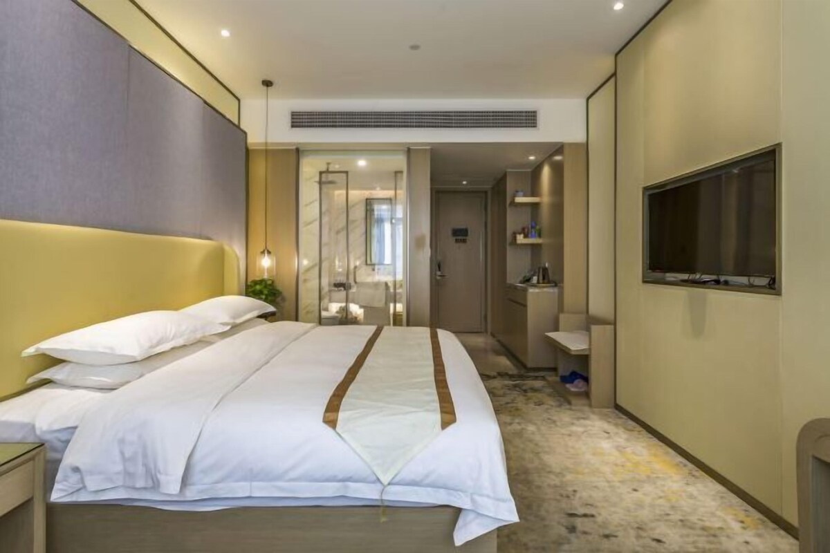 Habitación de hotel moderna con una cama grande, televisión, baño y un pasillo que conduce a otras habitaciones.