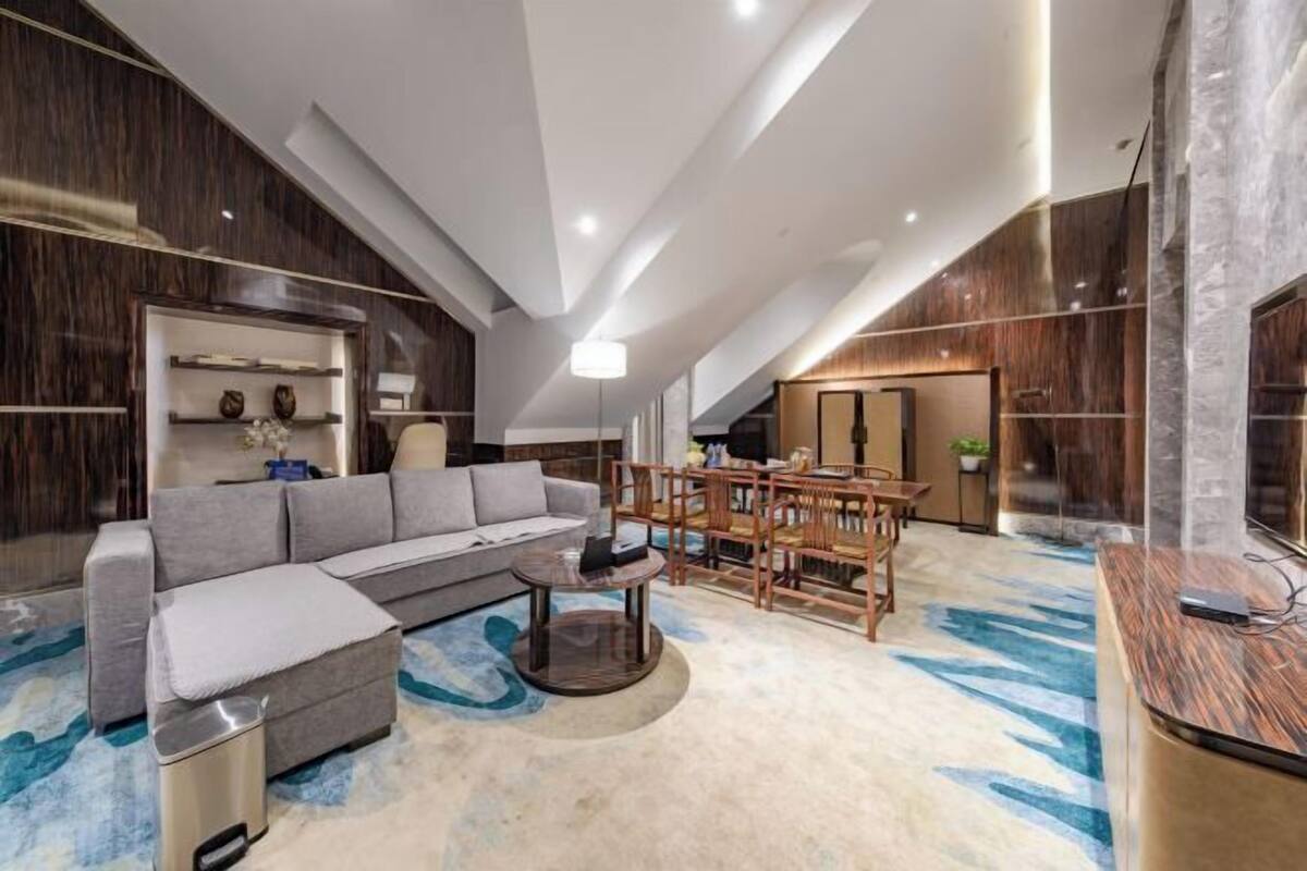 Uma sala de estar moderna com sofá, mesa de centro e área de jantar, com detalhes em madeira e piso de mármore.
