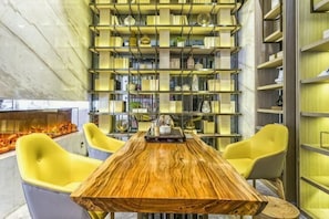 A modern interior with a wooden table, yellow chairs, and a wall of bookshelves.