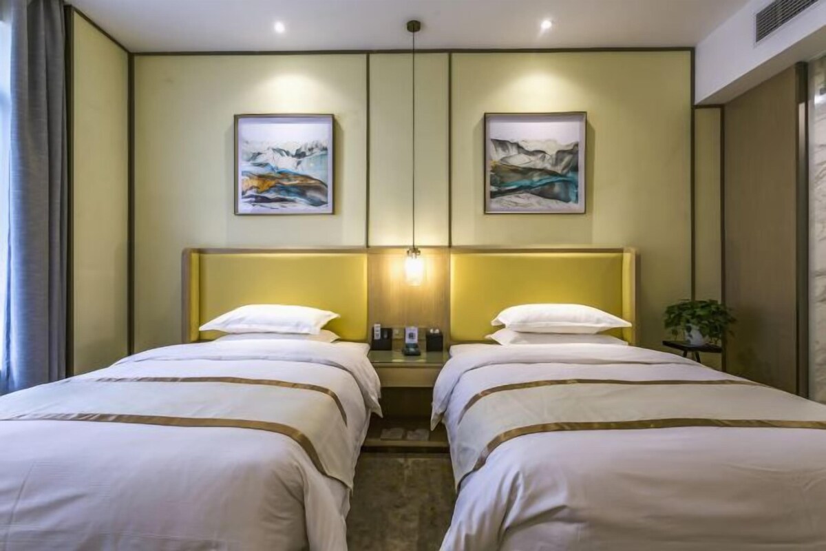 Une chambre d’hôtel avec deux lits, une tête de lit, des œuvres d’art accrochées aux murs, une table de chevet et une plante.