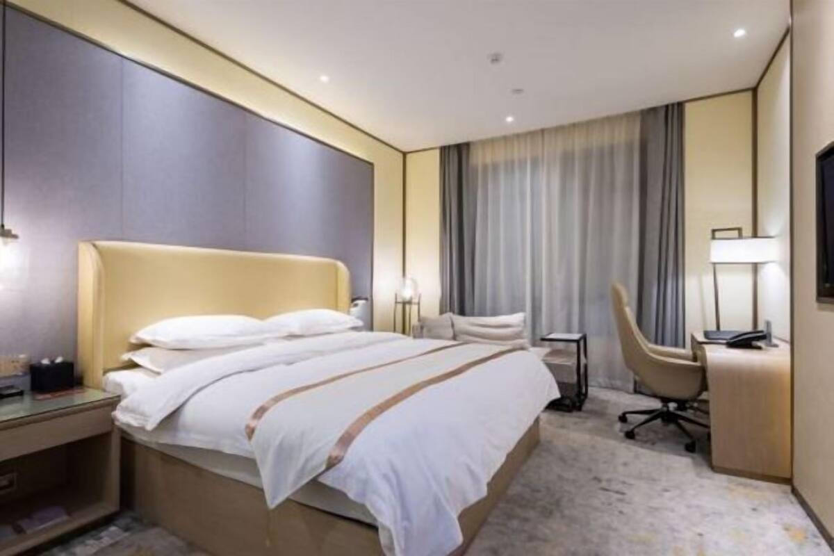Quarto de hotel com cama, escrivaninha, cadeira, televisão e abajur.