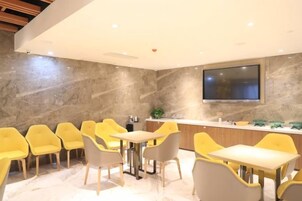 Un comedor moderno con una mesa larga y sillas amarillas, un televisor de pantalla plana en la pared y una pared de mármol.