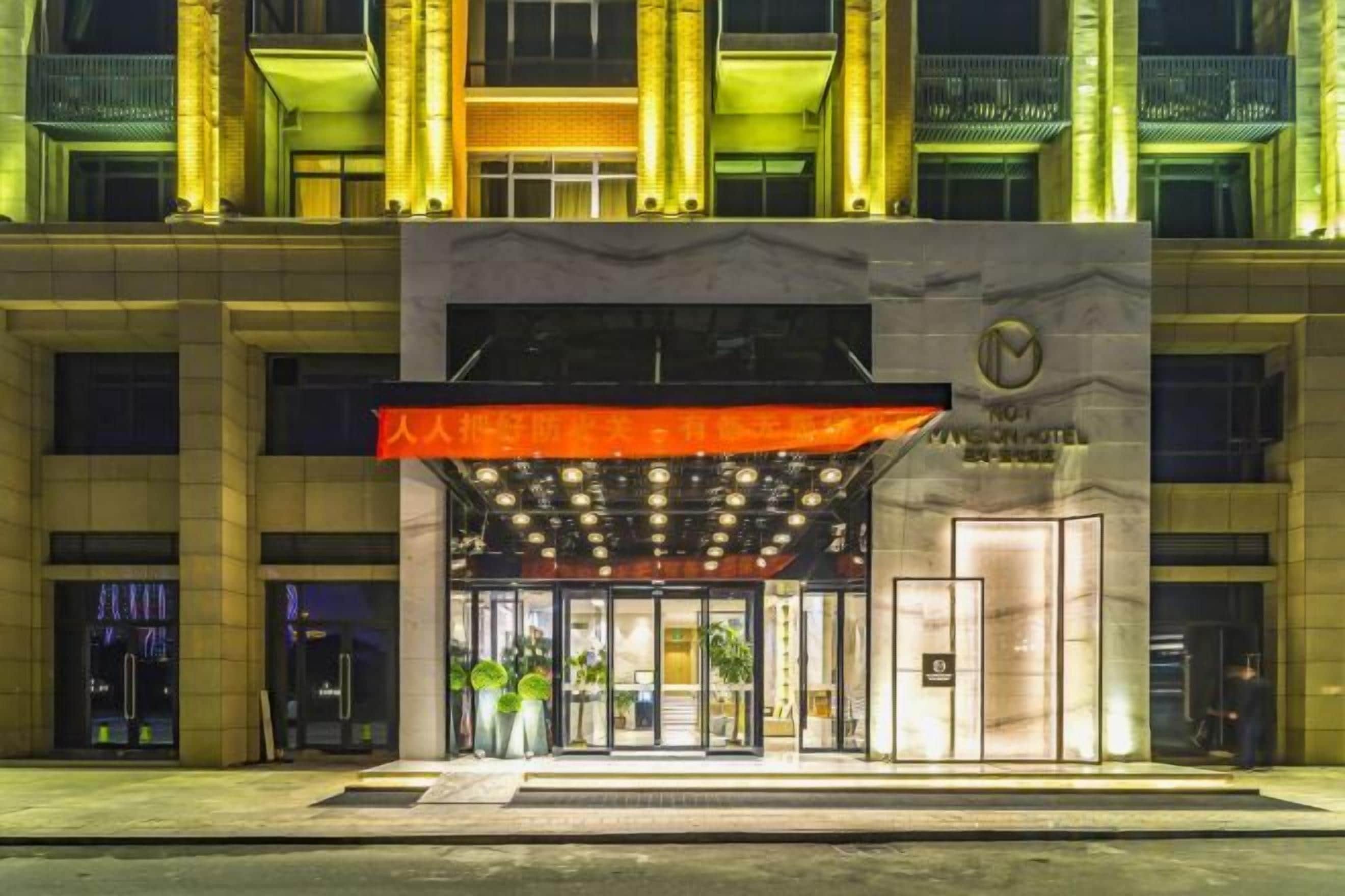 A hotel entrance with a prominent red awning, a large glass door, and a sign with a logo.