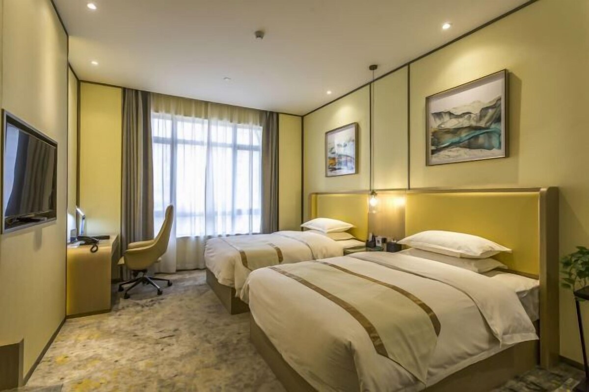 Habitación de hotel con dos camas, un escritorio, una silla, un televisor y obras de arte en las paredes.