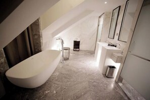 Un baño moderno con una bañera independiente, un tocador con espejo y un cubo de basura.
