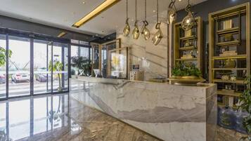 Zona de recepción de hotel con mostrador de mármol, puertas de vidrio y vista a automóviles estacionados afuera.