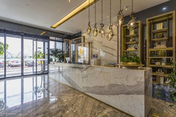 Zona de recepción de hotel con mostrador de mármol, puertas de vidrio y vista a automóviles estacionados afuera.