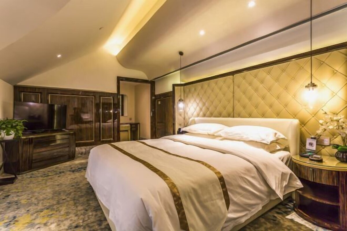 Un dormitorio con cama, televisor, cómoda y una mesa redonda con planta.