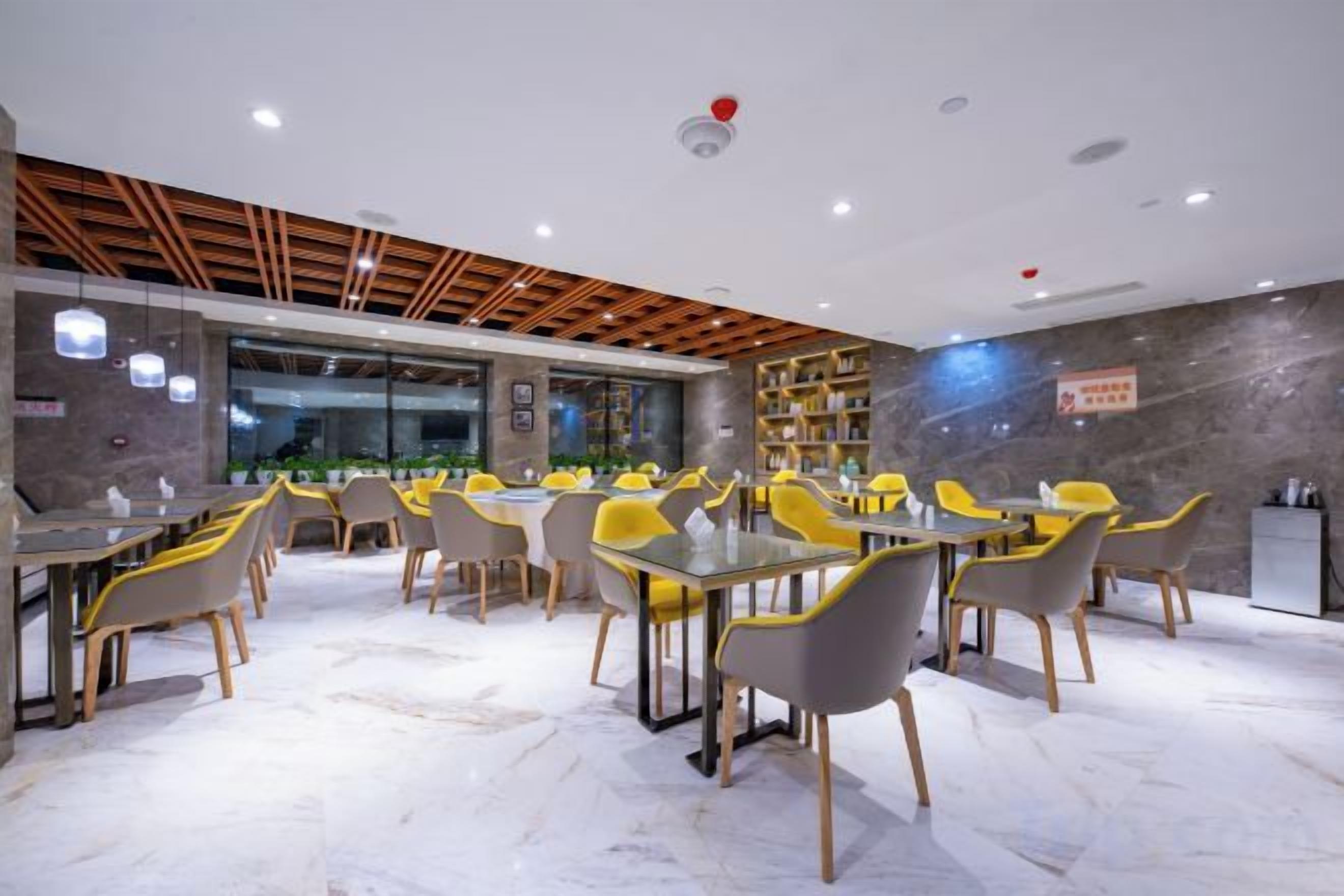 Un comedor moderno con mesas y sillas, una zona de cocina y vistas a través de un muro de vidrio.