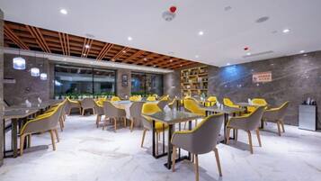 Un comedor moderno con mesas y sillas, una zona de cocina y vistas a través de un muro de vidrio.