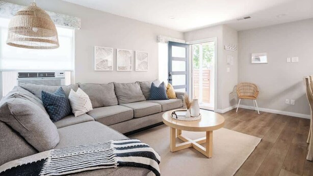 Un salon moderne avec un canapé d’angle gris, une table basse ronde en bois et une suspension en rotin.