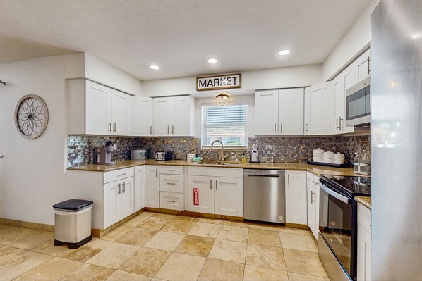 Kitchen features a clean design with white cabinetry, a tiled backsplash, and a large window.