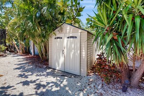 Situated in a lush garden, this charming shed offers a space surrounded by tropical plants and a gravel path.