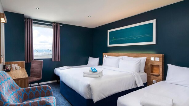 Une chambre d’hôtel avec un grand lit, un plus petit lit, une chaise, un bureau et une fenêtre avec des rideaux.