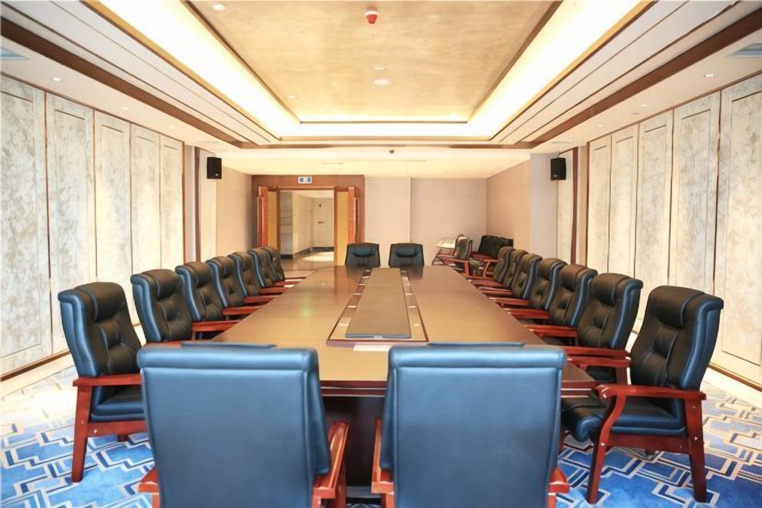 Sala de conferências com uma mesa comprida e cadeiras, carpete estampado e teto com iluminação embutida.