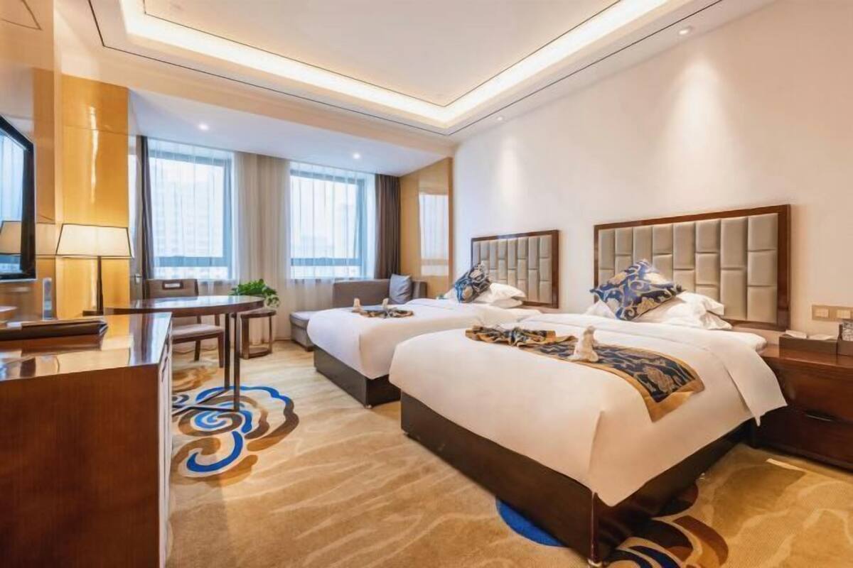 A hotel room with two beds, a desk, and a large window.