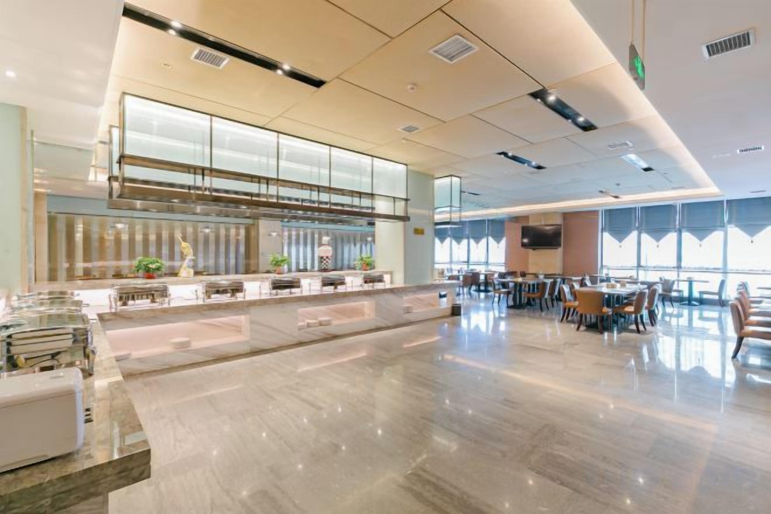 A spacious hotel lobby with a long reception desk, seating area, and large windows.
