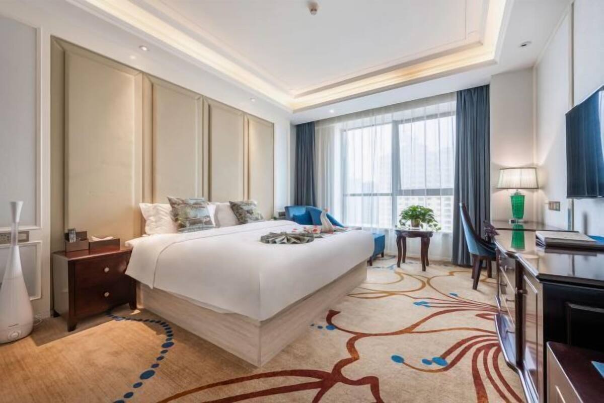 A hotel room with a large bed, a desk, a chair, a TV, and a window with curtains.