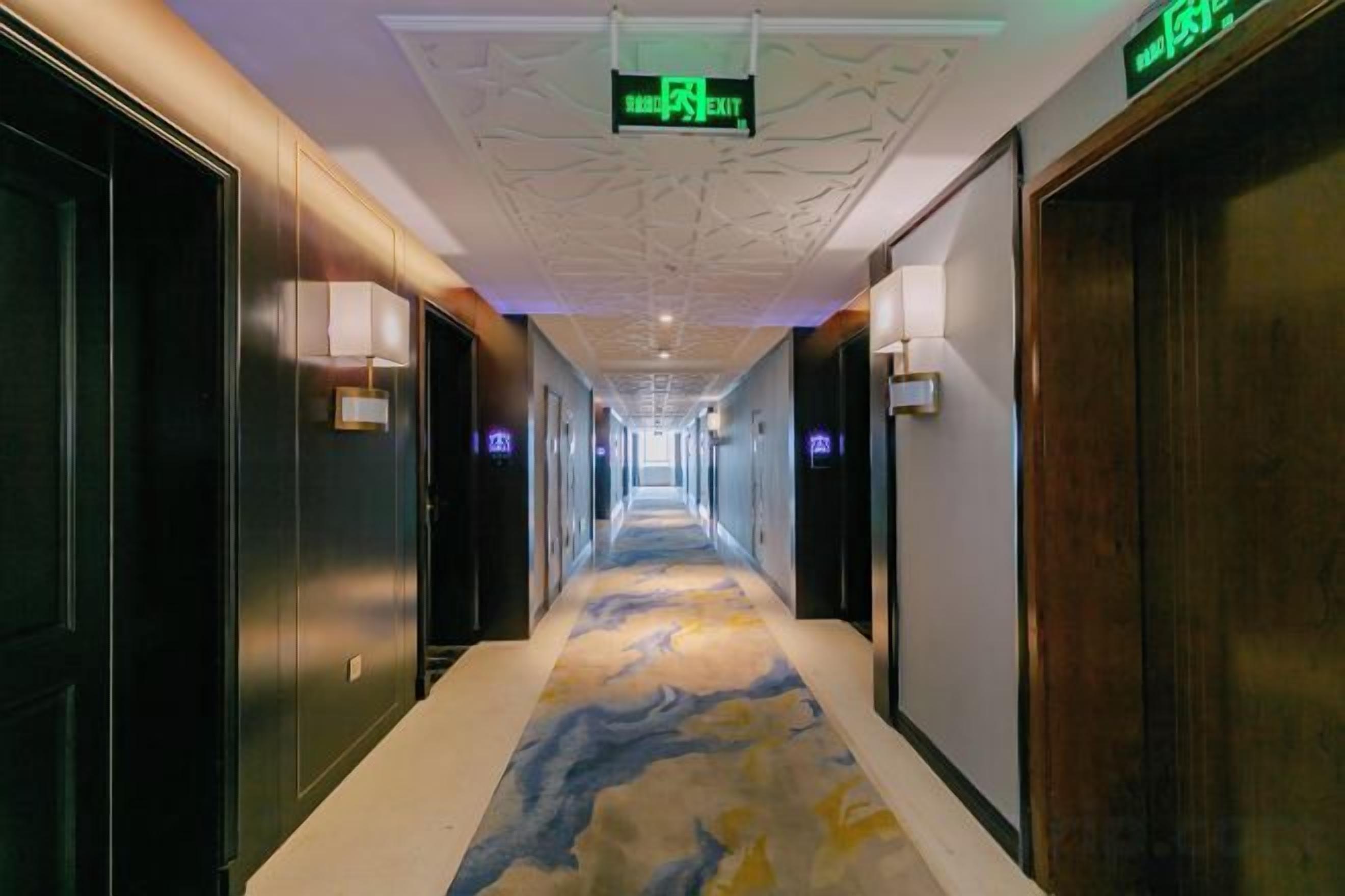 Un pasillo de hotel con alfombra estampada, luminarias fijadas a la pared y una señal de salida.