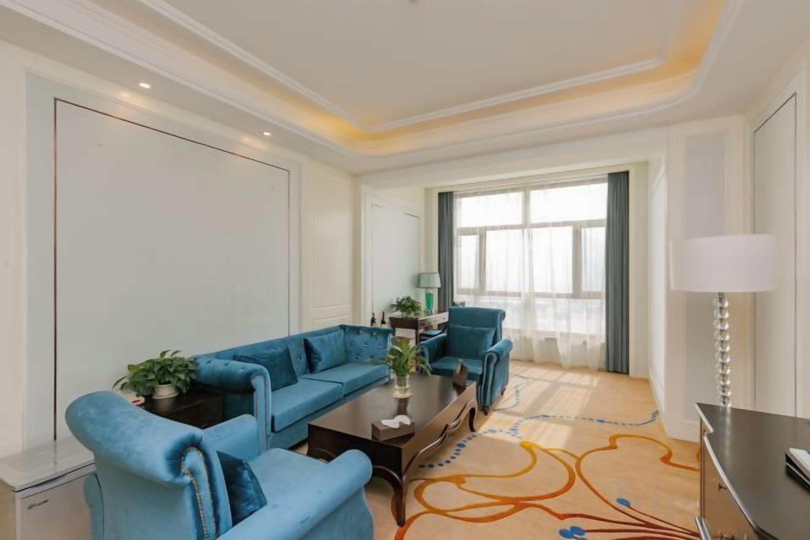 A modern hotel room with a blue sofa set, a dining table, and a TV.