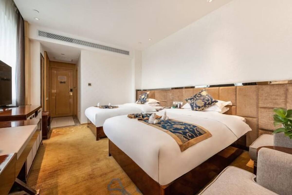 A hotel room with two beds, a desk, and a TV.