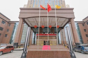 A building with a prominent entrance, large windows, and a red flag on a pole. - Hezhou Hongrui International Hotel (Linxia)